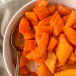 roast carrots in a white bowl with a serving spoon resting on the spoon with a beige napkin around the bowl