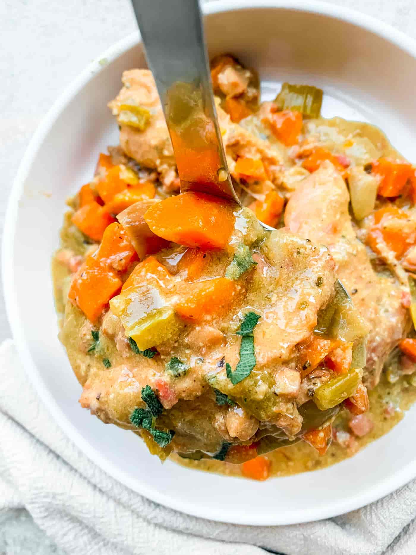 turkey casserole with celery, onion and carrot chunks on a ladle being held over a white dish full of the stew in the background