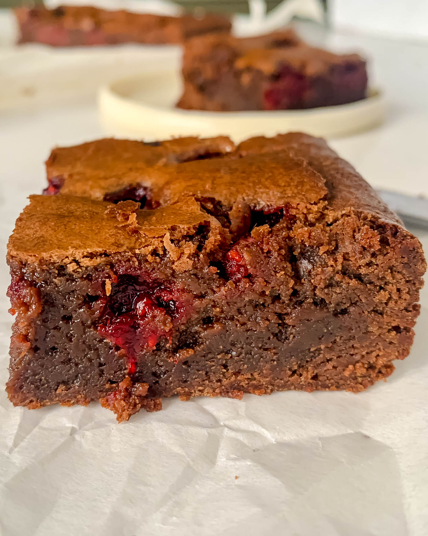 raspberry and chocolate brownies square on baking paper with another square in the background