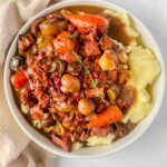slow cooker beef bourguignon on top of mashed potatoes in a round white serving dish with a beige napkin curled around the dish