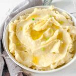 slow cooker mashed potatoes in a white round dish with a grey linen napkin curled around one side