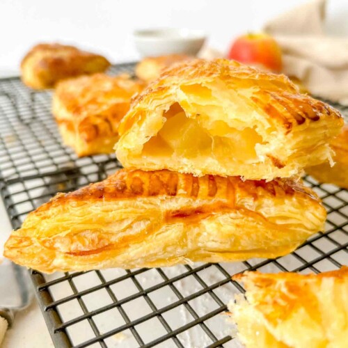 apple turnover cut open to show apple chunks on a metal cooling rack with an apple and beige napkin in the background