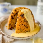 spotted dick with vanilla custard on a beige plate on a beige napkin with a spoon with custard on the side