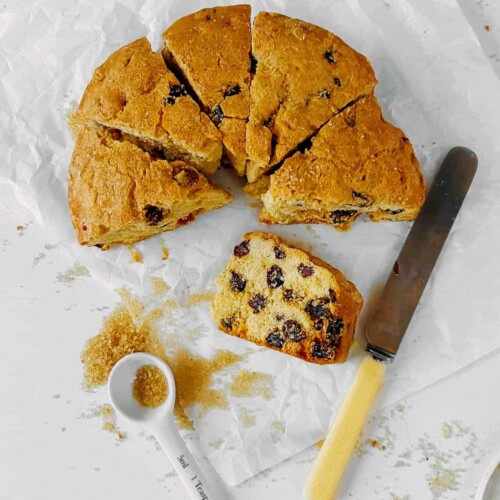 manor house fruit cake cut into wedges on white baking paper with one slice on it's side a teaspoon overturned filled with demerara sugar lying to the left and a yellow handled butter knife lying to the right