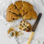 manor house fruit cake cut into wedges on white baking paper with one slice on it's side a teaspoon overturned filled with demerara sugar lying to the left and a yellow handled butter knife lying to the right