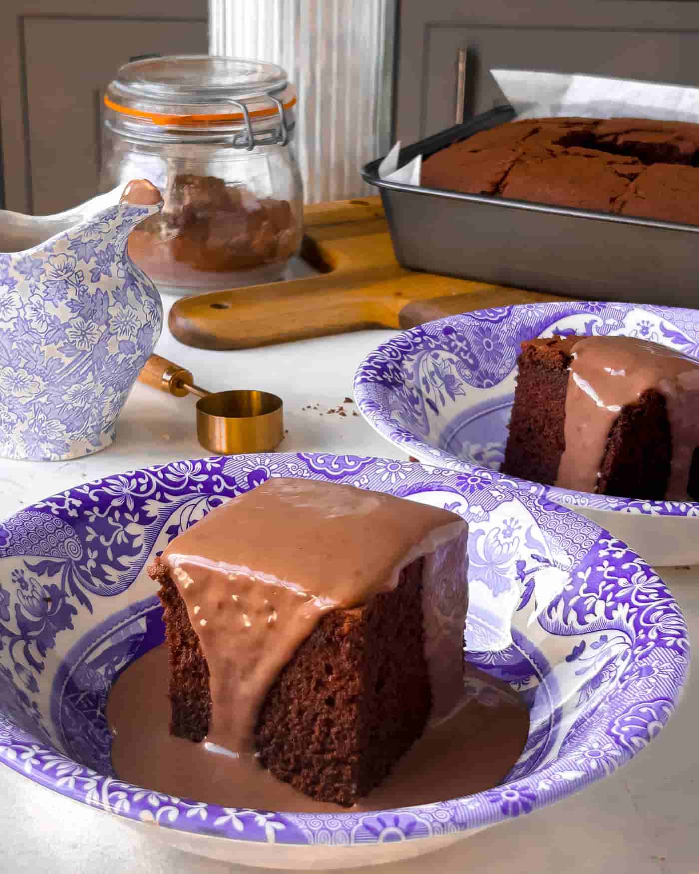 easy baked chocolate sponge pudding with chocolate custard in a blue and white bowl with another bowl with chocolate sponge and custard in it behind